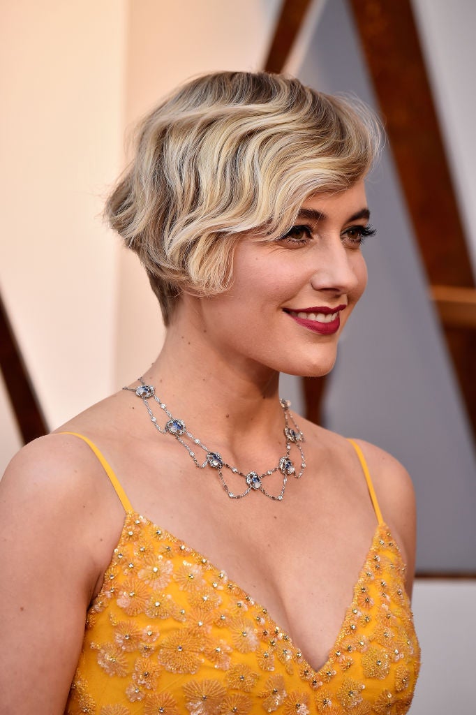 Greta Gerwig con pixie ondulado y un bonito maquillaje con labios burdeos y pestañas XXL.