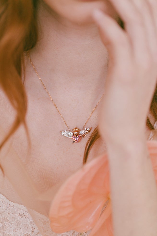 Colgante de oro y piedras preciosas con una espada de quita y pon que atraviesa el diseño del corazón.