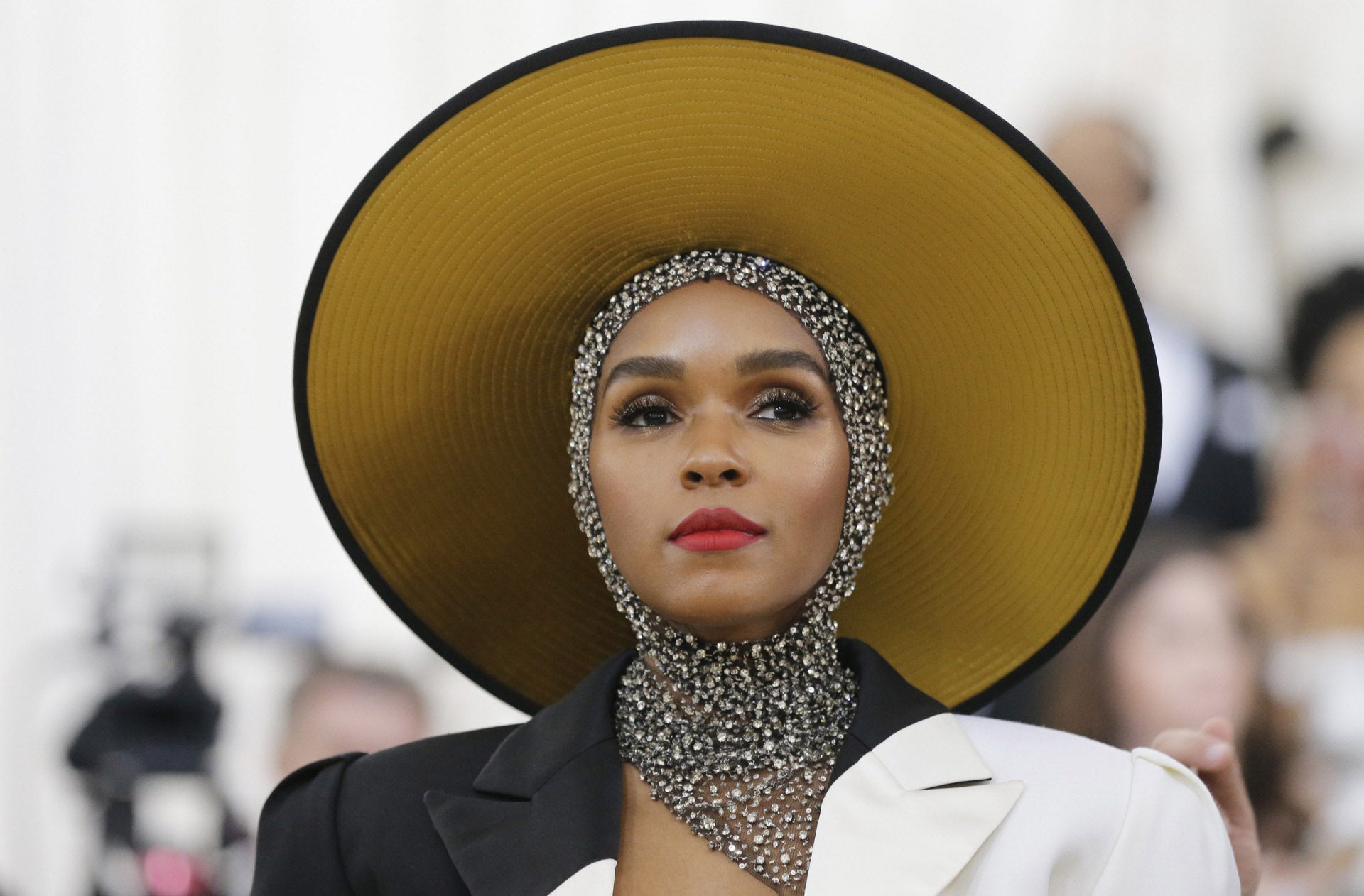 Más discretos es el tocado de Janelle Monae que cubrió su cabeza con una especie de mantilla de pedrería y encima una pamela XXL.