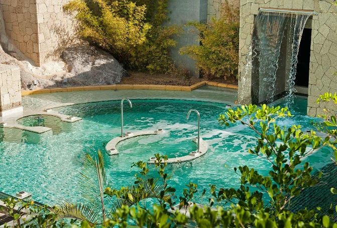 El Hotel Bahía del Duque situado en la Costa Adeje de Tenerife tiene un tesoro escondido: su spa. Disfruta de su circuito de talasoterapia en una piscina idílica rodeada de vegetación y una cascada de dos metros de altura. Su sonido relajante te transportará directamente al paraíso.