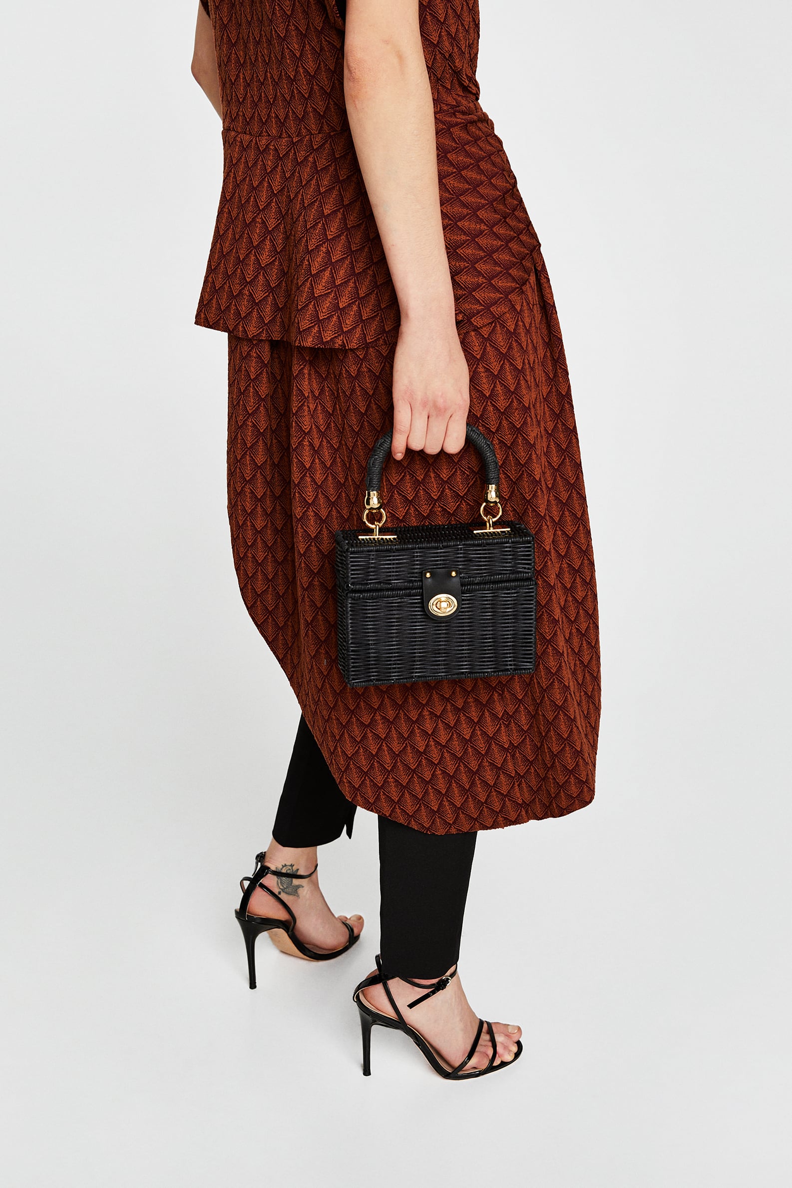 De rafia en negro. Una caja con asa de mano, cadena extraíble y metalería dorada, de Zara (25,94 euros).