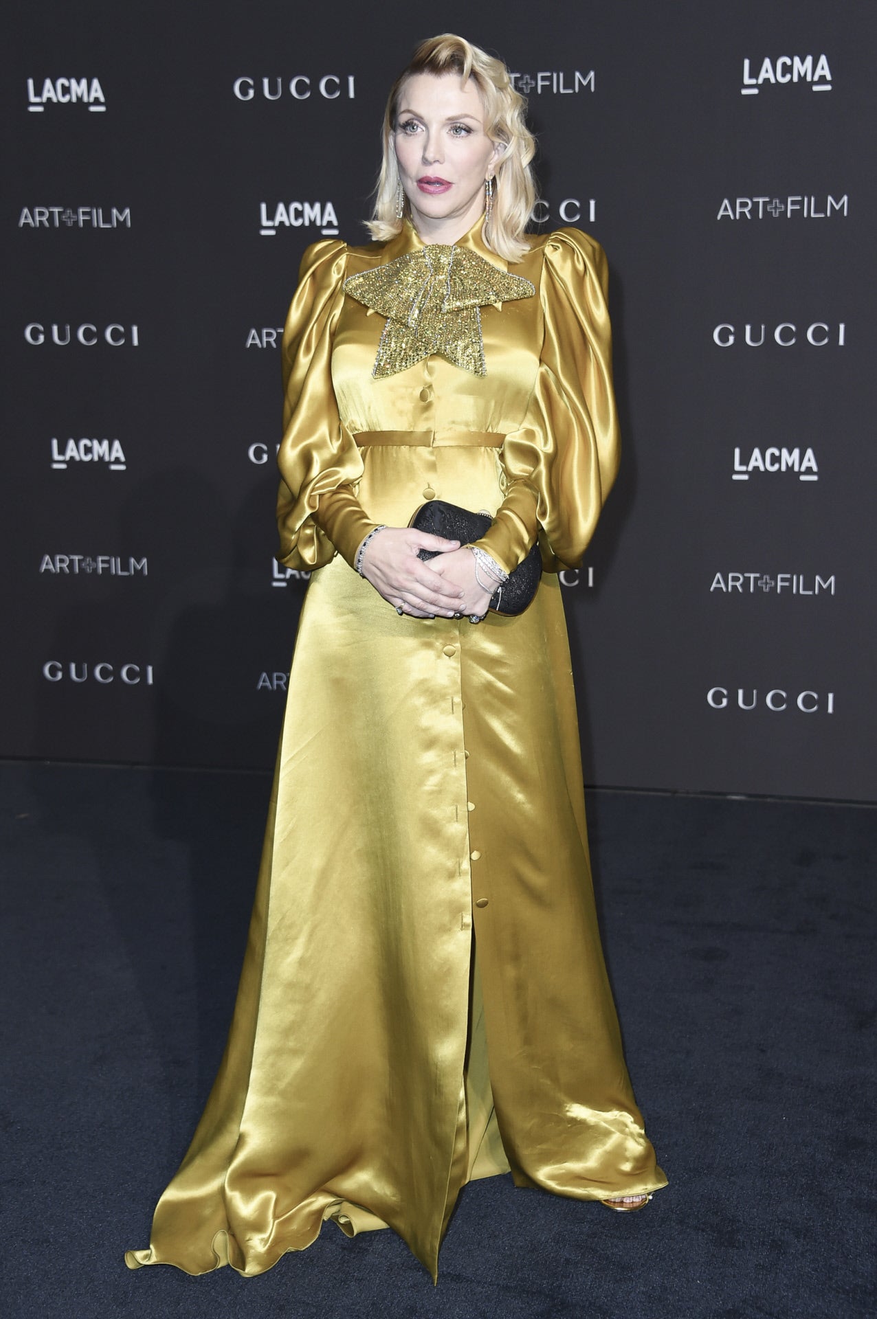 Courtney Love apostó por este Gucci dorado con gran lazo glitter y botonadura delantera, muy similar al que llevó  Dakota Johnson en los Oscar de 2017 .