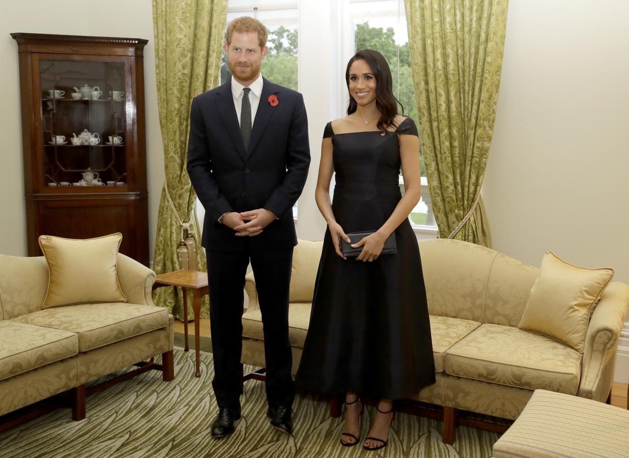 Vestido con corte en palabra de honor con mangas a los hombros en satén negro. Meghan es muy amiga de las gabardinas y es que es una prenda perfecta de entretiempo. En esta ocasión eligió un look en negro confortable con la gabardina en color gris topo.
