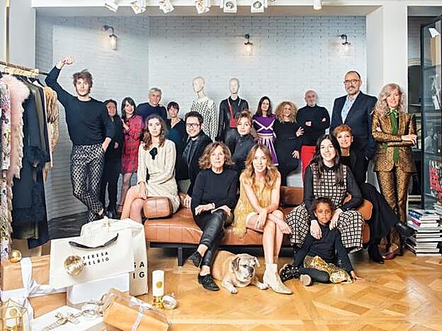 De pie, de izda. a dcha., Alejandro Andrés, asistente de diseño; María Flora, modista; Marta Domínguez, community manager; Nicusor Laza, sastre; Mari Angels Reverter, modista; Leire Gorrotxategi, showroom y ventas; Manuela Pino, modista; Joe Buj, maquillador y peluquero; Chema Paré, pareja de Teresa; y Liria Clement, patronista. Sobre el sofá, a la izquierda, Helena Ruiz, asistente en gestión de producto; Pol Guardiola, hijo de Teresa; delante, Teresa Blasco y su hija Teresa Helbig; detrás de ellas, Tatiana Voitekhovych, modista; dcha., Luz Sagalés, nuera y responsable de Comunicación; y la hija de Teresa, Zinash; detrás, Yolanda Bermúdez, responsable de gestión de producto.
