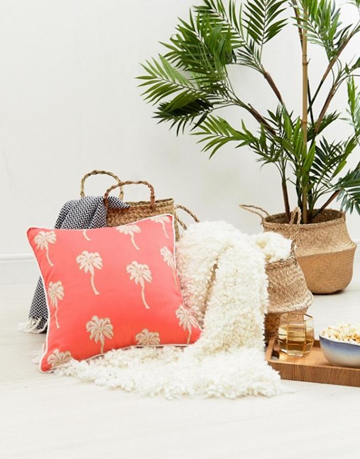 Este cojín con estampado de palmeras sobre fondo 'living coral' (color Pantone 2019) está rebajado a 33.99 euros en la sección de decoración de Asos.