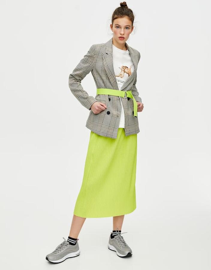 Falda midi plisada, con cintura elástica y silueta recta (29,99 euros), perfecta con la blazer de cuadros y un cinturón a juego ciñendo la cintura.