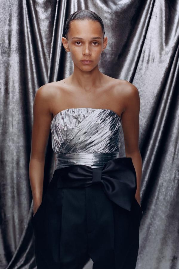 Top cropped plisado y plateado, con escote recto y tirante fino ajustable. Lleva un elástico en espalda y cierra en el lateral con una cremallera oculta en la costura (39,95 euros). Pantalones de tiro alto adornado con un gran lazo en la cintura. Lleva bolsillos delanteros y de doble vivo en la espalda (49,95 euros).