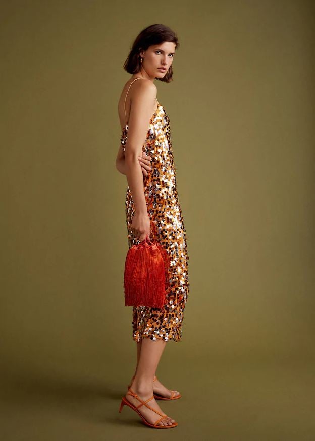 Otra de las joyas de la Gala Collection de Mango es este vestido midi de lentejuelas en tonos anaranjados (59.99 euros), que en el lookbook aparece combinado con una bombonera de flecos (49.99 euros) y unas sandalias de tiras en color naranja (59.99 euros).
