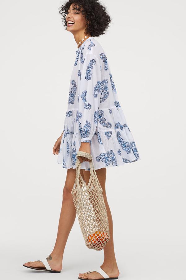 Túnica en tejido vaporoso de algodón con abertura con lazada en la parte superior. Modelo con hombros caídos, mangas amplias con puños estrechos con botón, costura fruncida en las caderas y parte inferior acampanada (29,99 euros).