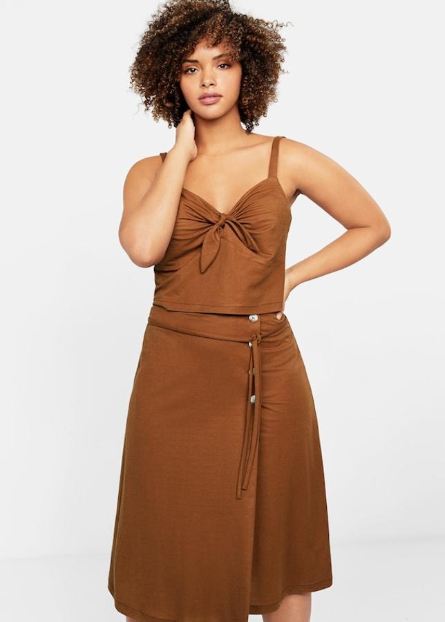 Lleva un falda midi con botones con un diseño acampanado y cruzado y bajo asimétrico (25,99 euros). Los botones son de carey y cierra con una cinta con lazo en la cintura. El top a juego lleva un lazo en el escote y tirantes (15,99 euros).