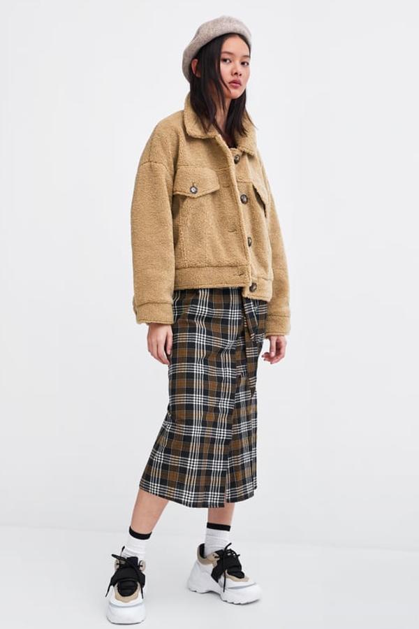 Cazadora amplia de cuello solapa y manga larga. Lleva bolsillos frontales de solapa y botón, bajo ajustable con trabilla y cierre delantero con botones (Zara, 25,99 euros).