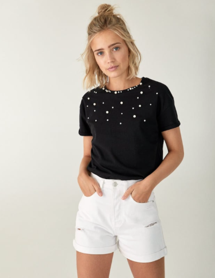 Camiseta negra adornada con perlas (12,99 euros) y shorto en denim blanco, con rotos estratégicos, silueta mom y bajo con vuelta (17,99 euros).