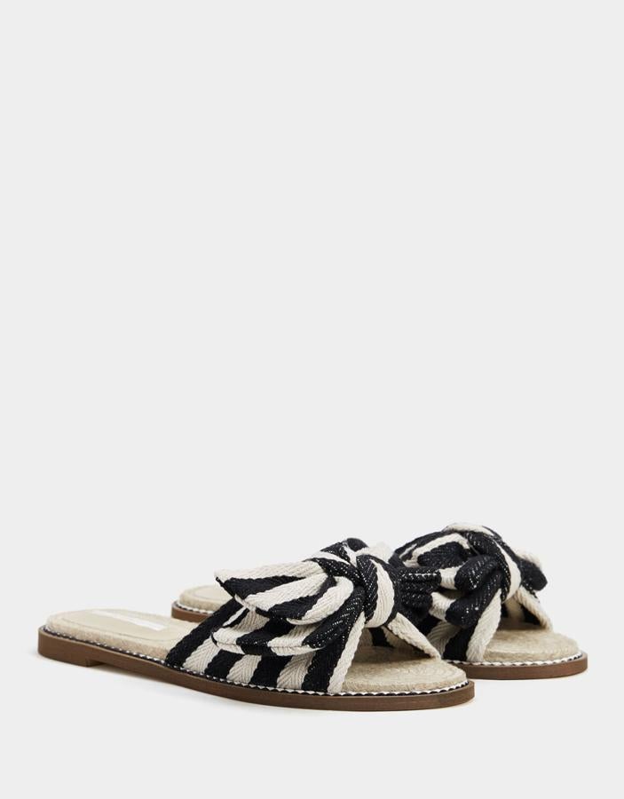 Sandalia plana en color negro y beige confeccionada en yute y con un lazo XL (Bershka, 9,99 euros).