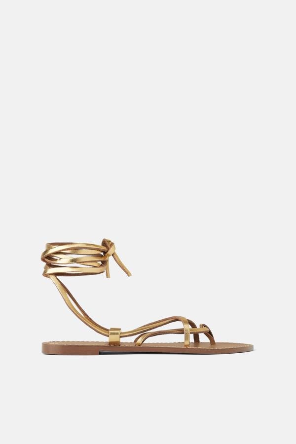 Sandalia plana de piel con tiras y una posición para el dedo. Llevan unos pespuntes en contraste de color en el contorno de la planta y cierran atándose al tobillo (Zara, 25,95 euros).