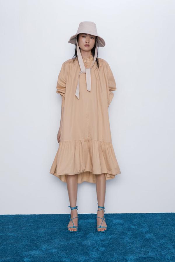Vestido amplio de el cuello subido y la manga larga, bolsillos laterales ocultos en costura y bajo asimétrico acabado en volante. Cierra en el frontal con abertura y botón (Zara, 39,95 euros).