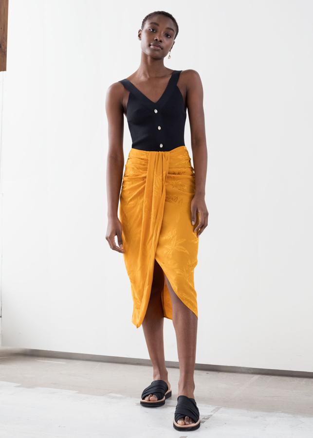 Esta falda midi en satén estampado a tono en amarillo curry con silueta pareo podría ser de Jacquemus, pero es de la nueva colección de &Other Stories, cuesta 69 euros, y además de ser preciosa, marca la cintura, disimula la tripita y hace las piernas más largas gracias a su abertura delantera.