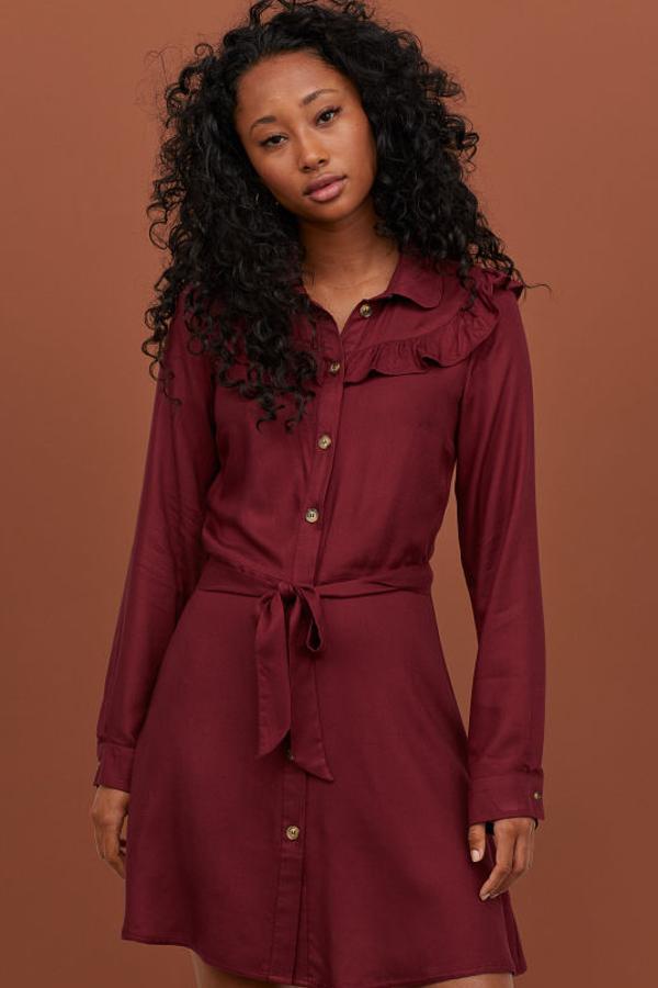 Vestido camisero corto en sarga ligera de viscosa, con cinturón de anudar extraíble. Lleva cuello redondeado, canesú con ribete de volante, cierre de botones y mangas largas con botón en los puños. Va sin forrar (H&M, 29,99 euros).