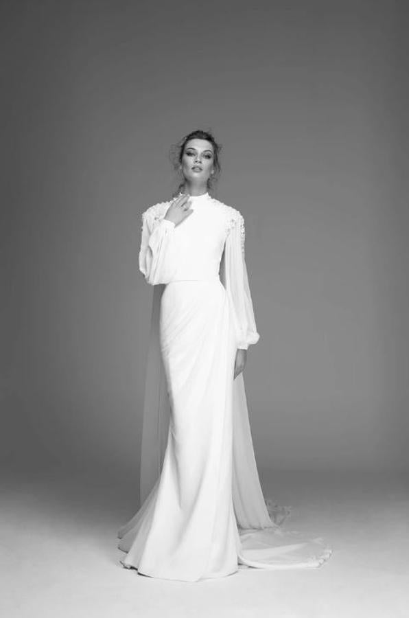 Vestido confeccionado en crepé con cuello subido, mangas abullonadas de gasa y sobrefalda cruzada del mismo tejido. Aplicación bordada de flores en los hombros.