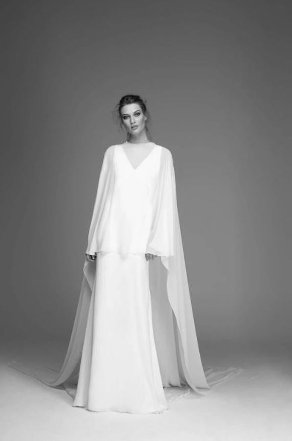 Vestido de crepé con escote de pico y manga a la sisa, con una capa de gasa con escote a la caja con una larga cola y decoración de cristal en los hombros y escote.