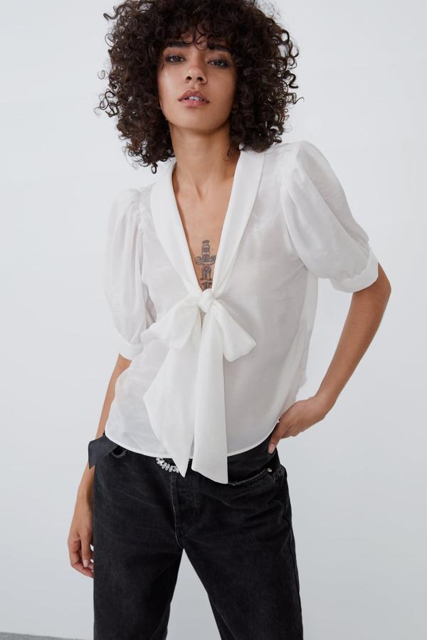 Camisa fluida de escote pico y manga corta abullonada de Zara (25,95 euros). Lleva el detalle romántico del lazo en la pechera.
