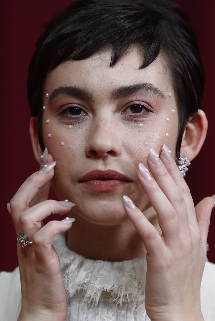 Greta Fernández ha brillado con un maquillaje creado por David Bello para Chanel e inspirado en la belleza clásica de Audrey Hepburn: piel natural con pecas, labio nude efecto mordido y afrutado y el glamour de las perlas alrededor de su mirada y en su manicura.