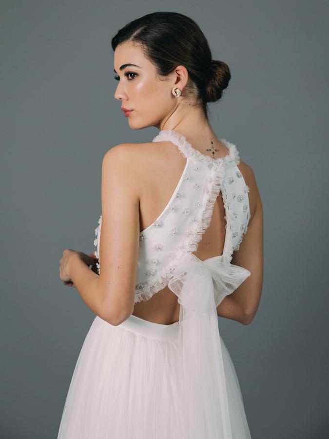 Vestido de novia con cuerpo confeccionado en crepé cubierto en tul de fantasía. Detalles de carrucha y fina pedrería. Favorecedor lazo de fino tul en la espalda. Corte en la cintura y voluminosa falda de tul, sin cola.