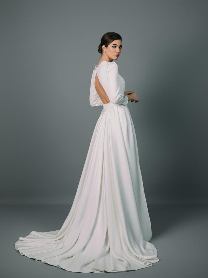 Vestido de novia con museta y escote reina, manga francesa y cuerpo entallado. Corte en la cintura y falda de capa sin cola. El vestido se complementa de una cola postiza abrochada con cinturilla. Confeccionado en tejido con textura de piel de elefante con detalles de cristales.