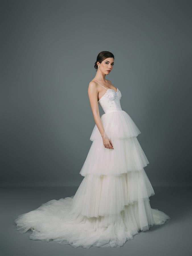 Vestido de novia con corpiño entallado confeccionado en crepé y forrado con tejido fantasía. Corte en la cintura y voluminosa falda de volantes con cola confeccionada en tul fino.