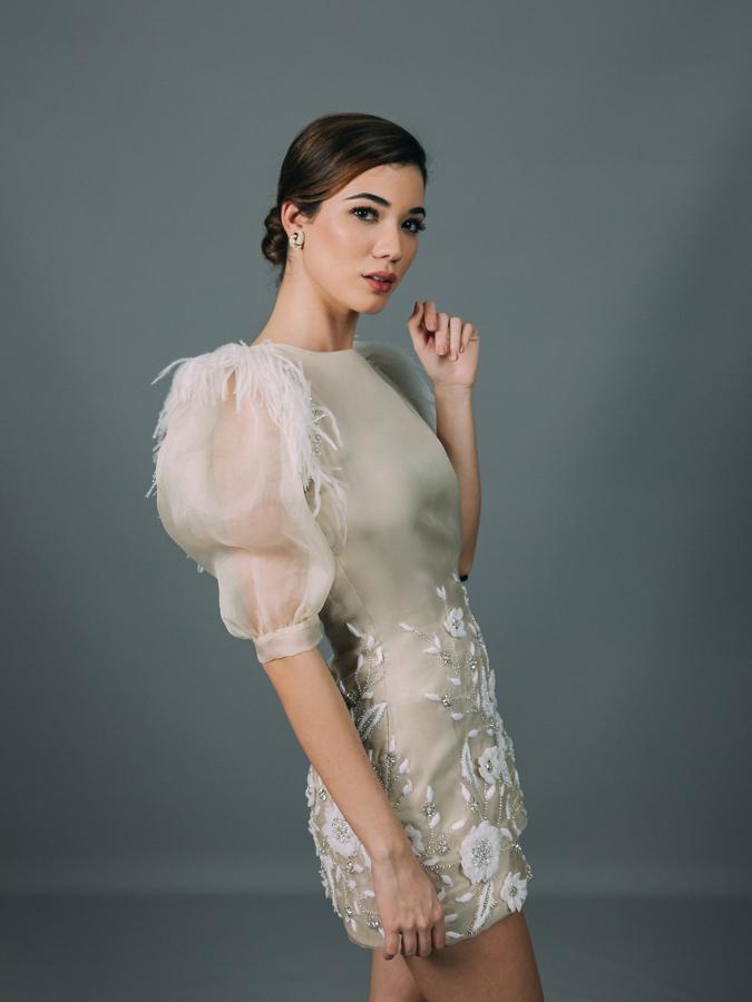 Vestido de novia corto, confeccionado en tejido de organza bordada en cristal, voluminosas mangas farol con detalle de plumas y pasamanería en el hombro.