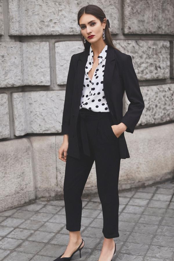 Camisa manga larga de lunares (9,99 euros), blazer negra con botones (25,99 euros), jogger de pinzas con cinturón (14,99 euros), diadema trenzada (3,99 euros) y pendientes de perlas (2,99 euros).