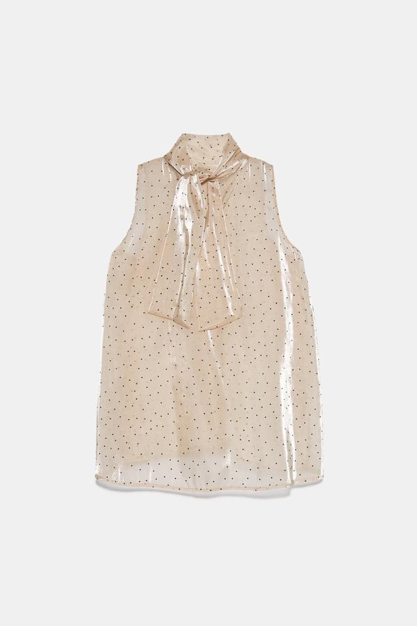 Cuello subido y manga sisa para este precioso top semitransparente en tonos crudos con lunares y lazo al cuello. Cuesta 22,95 euros y está disponible entre las tallas XS y XL.