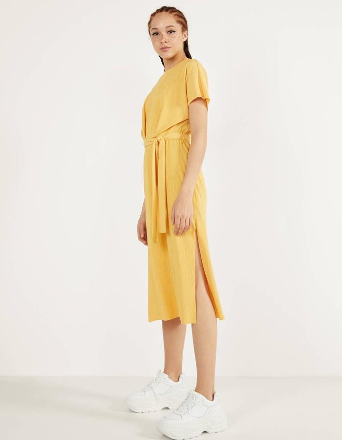 Este vestido midi de manga corta en color mostaza de Bershka. También está disponible en negro, azul y azul claro, y tiene un cinturón de tela para ajustar a la cintura. Puedes encontrarlo de la talla XS a la L y tiene un precio de 19,99 euros.