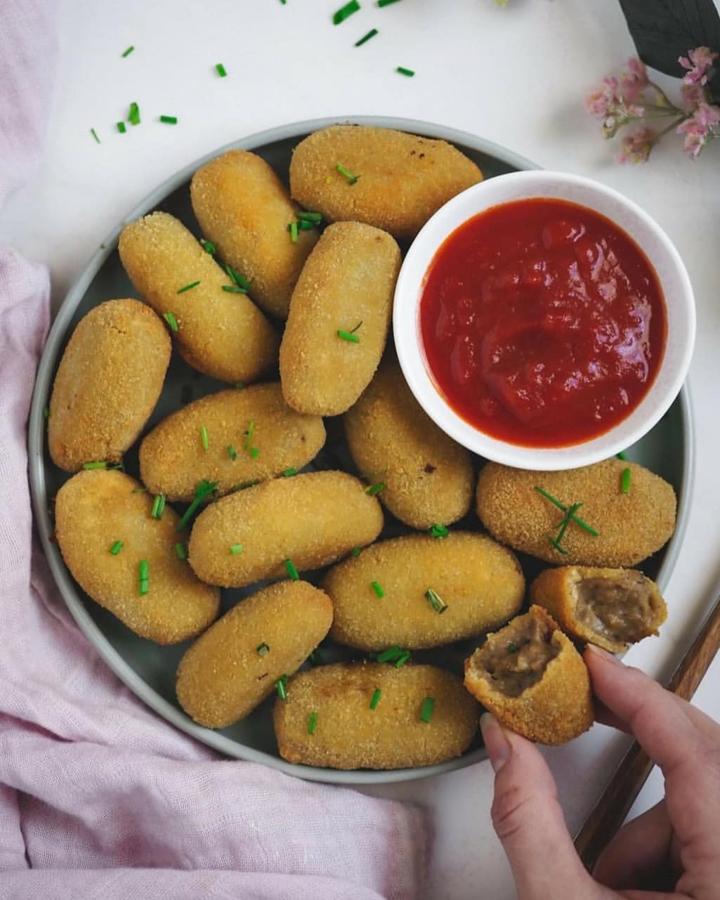Ingredientes para la masa (20 croquetas):1 cebolla1 ajo450 gr de setas variadas congeladas80 gr de harina de trigo (40 gr de maicena para hacerla sin gluten150 ml de bebida de sojaUna pizca de salPimientaNuez moscadaAOVEIngredientes para el rebozado:4 cucharadas de harina de garbanzo200 ml de agua1 pizca de sal1/2 cucharadita de vinagre de manzanaPan ralladoHarina de trigo (vale cualquier otra)Preparación:- Cortamos el ajo y la cebolla muy finamente y los pochamos muy finamente y los pochamos en una cacerola con un poco de AOVE y una pizca de sal.- Una vez pochados, añadimos las setas, que previamente habremos descongelado y picado de forma muy menuda. Cocinamos hasta que las setas no suelten más agua.- Echamos la harina y seguimos cocinando sin dejar de remover durante 3 minutos.- Incorporamos la sal, la pimienta, la nuez moscada y la bebida de soja y cocinamos, sin dejar de remover, hasta que la masa espese bien (unos 3-4 minutos más). Si quedan grumos en la masa, podemos pasar la batidora)- Ponemos la masa en una fuente grande y la extendemos. Le ponemos un poco de AOVE por encima, la tapamos y la dejamos enfriar a temperatura ambiente.- Dejamos que repose en la nevera 4-5 horas como mínimo.- Le damos forma a las croquetas y las ponemos sobre una bandeja con un poco de harina.- Hacemos la mezcla del no huevo poniendo en un bol la harina de garbanzo, la sal, vinagre y agua. Batimos bien.- Pasamos cada croqueta por esta mezcla y luego la rebozamos bien con el pan rallado. Para una croqueta extra crujiente, haremos este proceso del no huevo más el pan rallado dos veces. Si la mezcla de no huevo se espesa, podemos añadir agua.- Freímos las croquetas en AOVE caliente y las sacamos sobre papel absorbente. También las podemos hornear a 200ºC hasta que queden doradas.