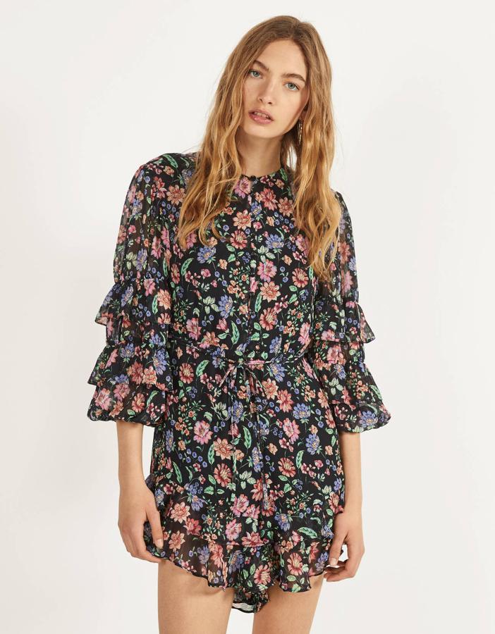 En tejido de gasa, con fondo negro y estampado de flores, este mono corto de Stradivarus tiene detalles de volantes tanto en las mangas como en el bajo del pantalón (29,99 euros).