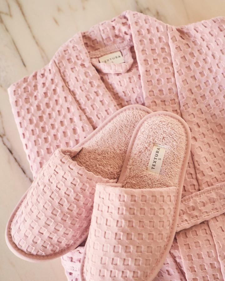 La textura gofre llega a las zapatillas y al albornoz en múltiples colores. Albornoz rosa, (49,99 euros).