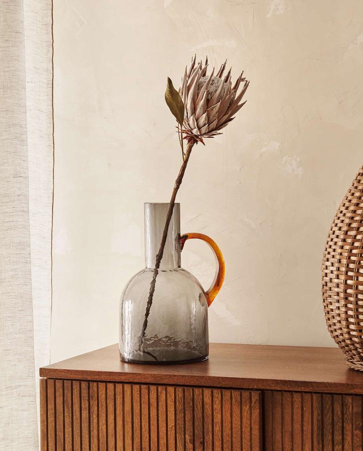 Este original jarrón de vidrio gris con asa en tono marrón tiene un precio de 19,99 euros y es apto para contener agua.