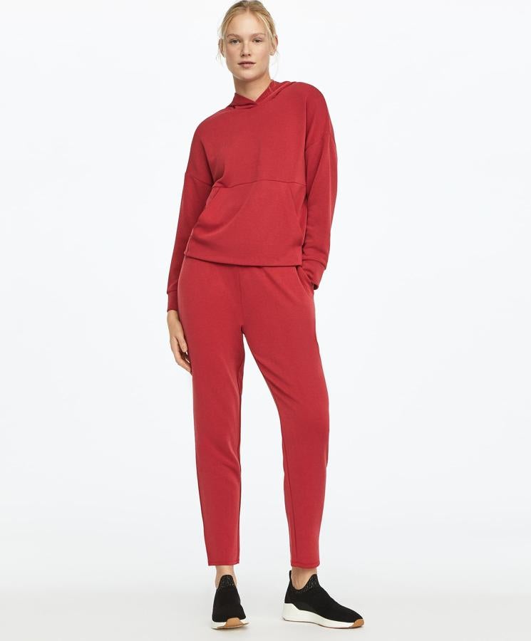 En color rojo, con opción en negro o gris, esta sudadera con capucha ajustable y bolsillo frontal es de Oysho. De tejido suave, está actualmente rebajada y tiene un precio de 20,99 euros. Puedes encontrar el pantalón a juego.