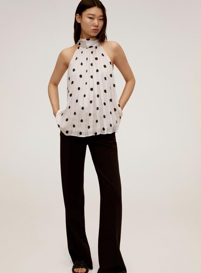 Este top plisado en color blanco con topos en negro es de Mango y está actualmente rebajado. Con cuello halter y cierre de lazo en el cuello, tiene un precio de 22,99 euros.