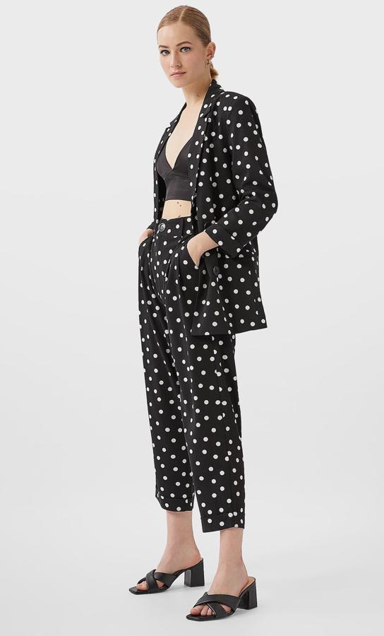 Este traje de chaqueta y pantalón negro con topos blancos es de Stradivarius. La americana con doble botonadura tiene un precio de 29,99 euros y el pantalón fluido 19,99 euros.