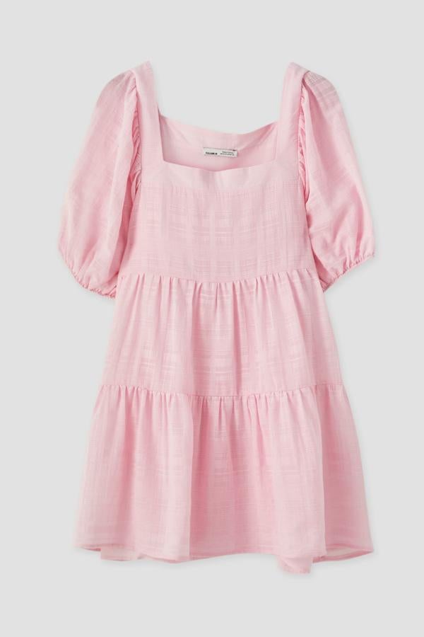 En color rosa, este vestido de corte babydoll con escote en forma de caja está confeccionado en algodón. De manga corta, tiene un precio de 25,99 euros.