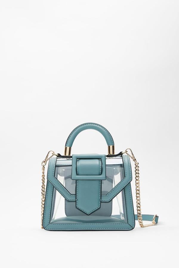 En color azul, este bolso en formato mini city con cuerpo de vinilo transparente y detalle de hebilla en la solapa tiene un precio de 25,95 euros. Cuenta tanto con asa de mano con detalle dorado como con asa de hombro con cadena dorada.