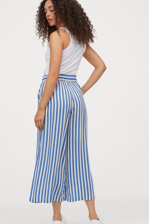 Este pantalón tobillero de rayas en blanco y azul está también disponible en otros colores. En tejido fluido con perneras amplias de corte recto, tiene un precio de 14,99 euros