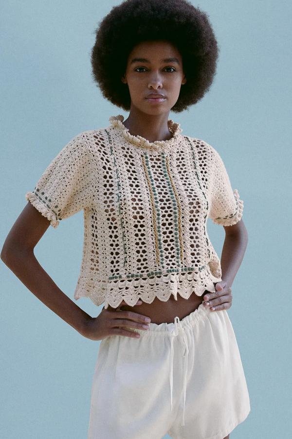 En color crudo, este top de crochet de manga corta con cuello redondo cuenta con acabado en volantes. Con cierre en la espalda con abertura y botones, es de Zara y tiene un precio de 29,95 euros.