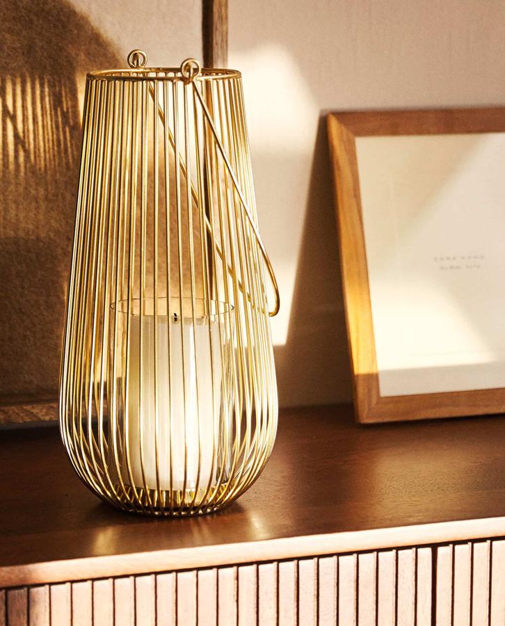 Este farolillo realizado con alambres de metal en color dorado cuenta con asa para transportarlo y tiene un precio de 39,99 euros.