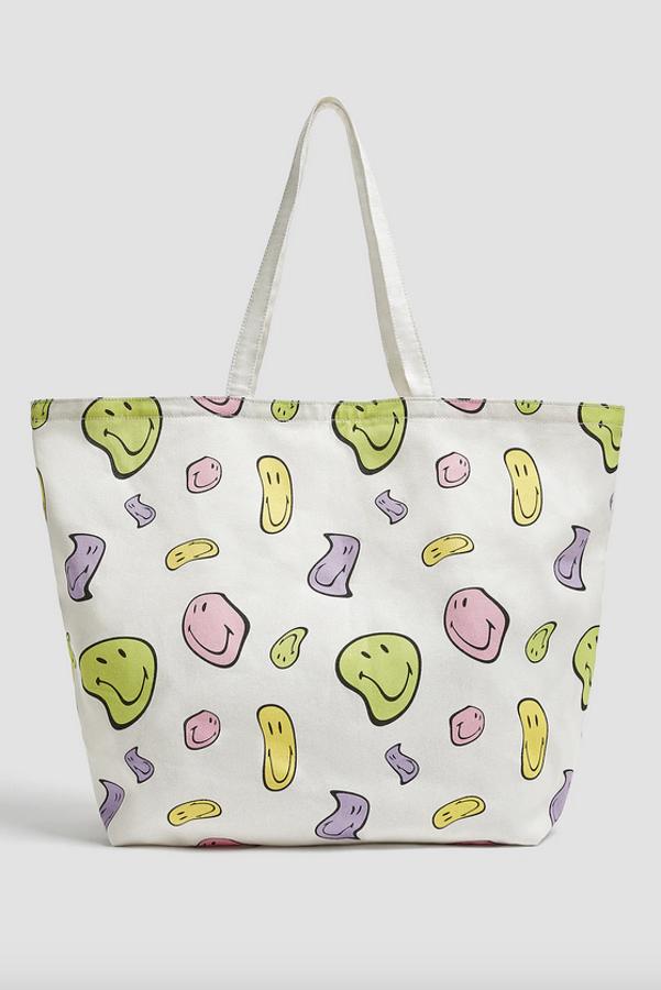 Entre los accesorios de esta colección cápsula podemos encontrar este simpático bolso tipo shopper en color blanco con print de Smiley multicolor con asas de hombro. Cuesta 25,99 euros.