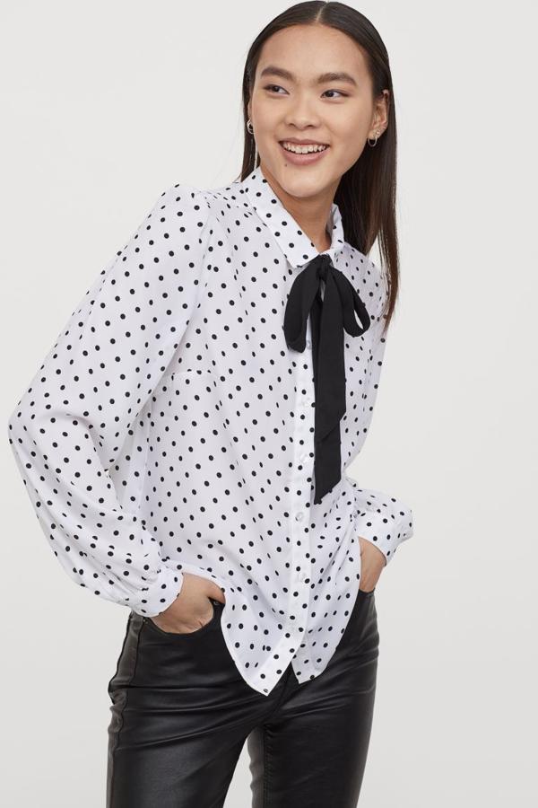 Camisa vaporosa con cuello y lazada cosida en color negro para esta camisa en color blanco con lunares negros de H&M. De 19,99 euros ha pasado a 9,99 euros y está disponible entre las tallas 32 y 40.