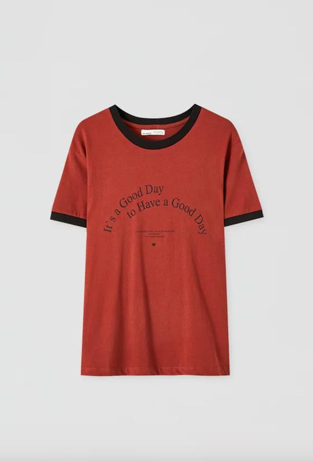 En rojo teja con mangas y cuello en negro, esta camiseta de Pull&Bear invita a afrontar el día con optimismo, porque siempre “es un buen día para tener un buen día. Cuesta 5,99 euros y está disponible únicamente en la talla L. Y se está agotando.