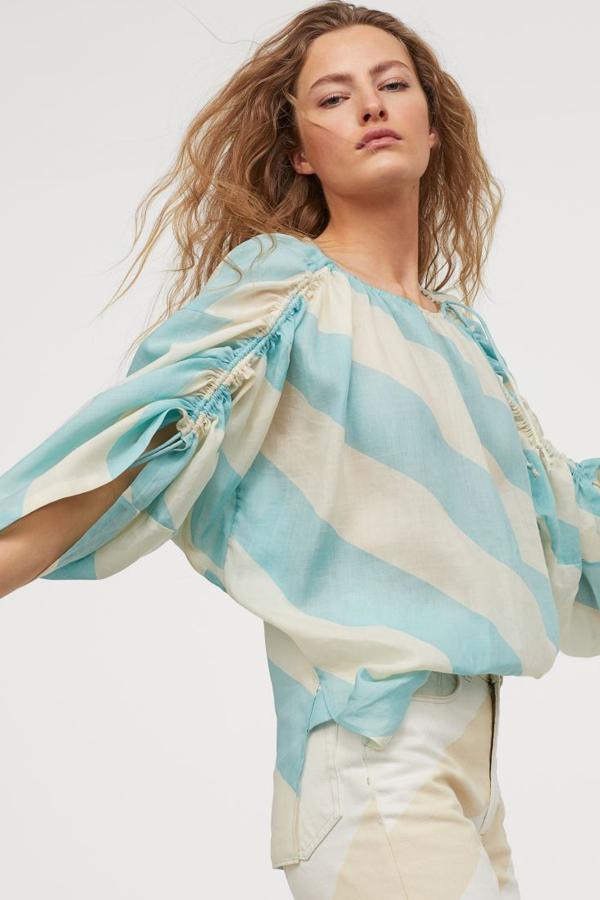 Blusa voluminosa en ramio vaporoso con aberturas pronunciadas en los laterales. Lleva escote holgado con cordón de ajuste y mangas dolman tres cuartos de corte amplio con fruncidos y cordón de ajuste con tiras largas de anudar. Es de la colección Studio Collection y cuesta 59,99 euros.