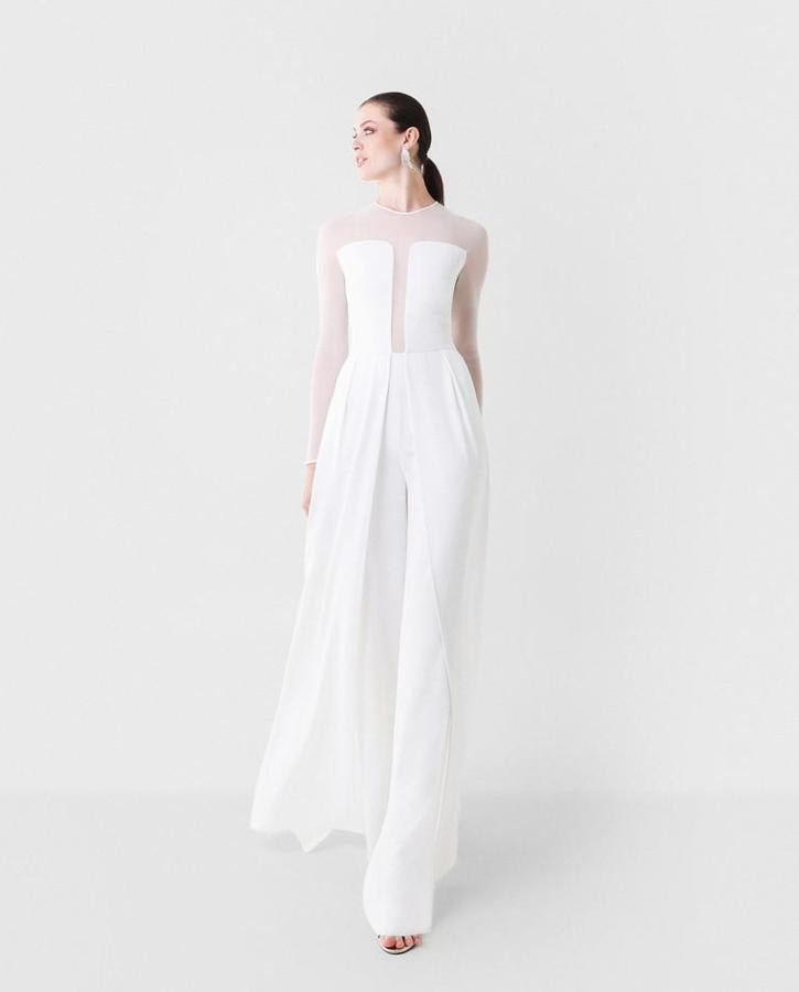 Mono de invitada de crepé y tul elástico en color blanco. Las mangas y centro del cuerpo delantero en tul translucido crean un efecto fresco y colorido a la par que diferencial. Su corte en la cintura y pantalón recto estilizan la figura junto con su sobrefalda plegada que aporta movimiento y fluidez al look. Rebajado de 290 a 203 euros.