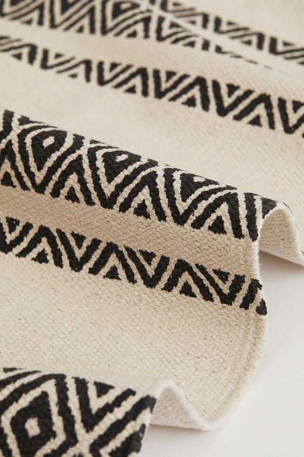 Esta alfombra en tejido de algodón con estampado en tonos blanco y gris tiene unas medidas de 70x140 centímetros. Su precio rebajado es de 10,99 euros.